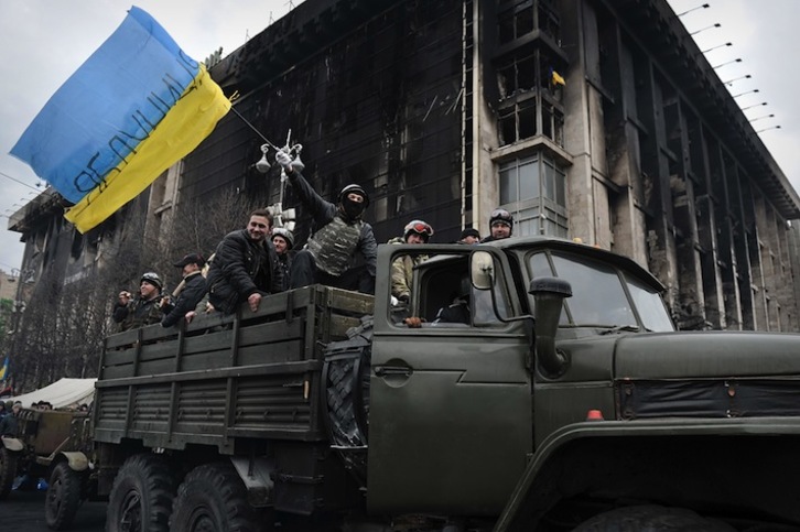 Un grupo de opositores ondea la bandera ucraniana en un vehículo militar. (Louisa GOULIAMAKI/AFP) 