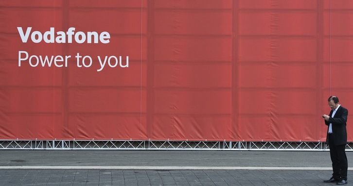 Un hombre consulta su teléfono móvil frente a un cartel de Vodafone. (John MACDOUGALL/AFP)