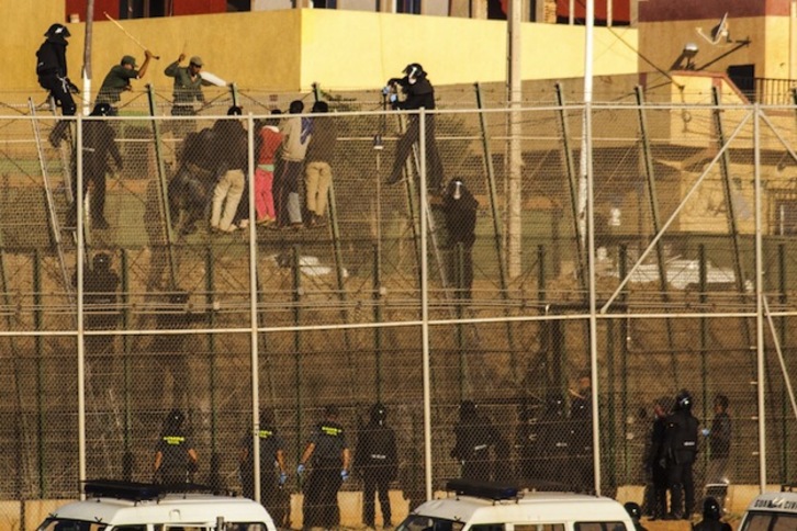 Agentes españoles y marroquíes, estos últimos con bastones, se encaraman a la valla para hacer bajar a la fuerza a los inmigrantes. (José COLÓN / AFP)